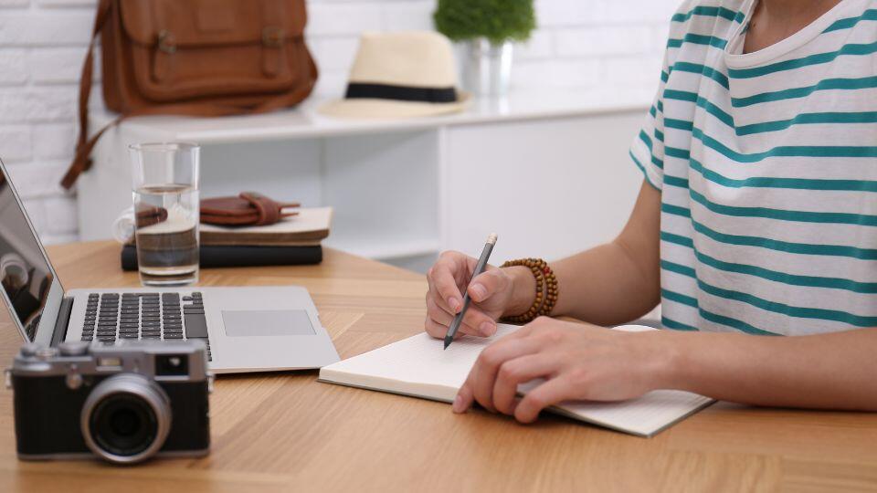 person sitting at a desk with laptop, camera and pen