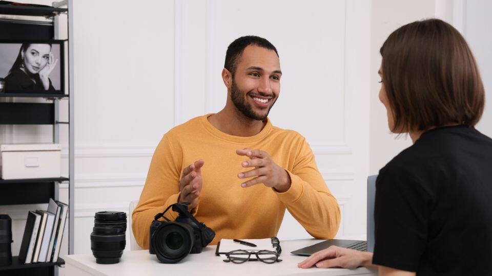 a photographer sitting at a desk talking to another professional