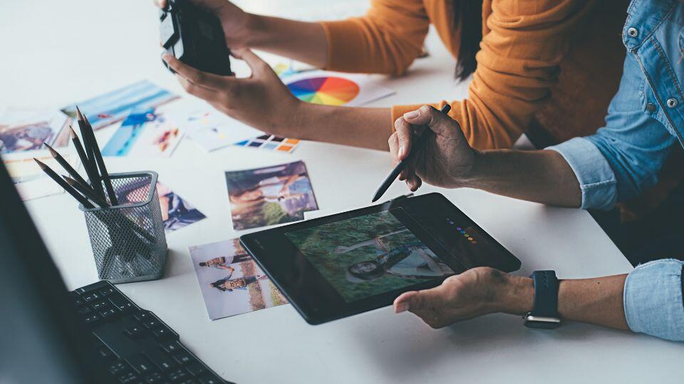 two people sitting at a table with a tablet and camera