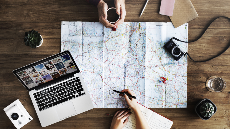 Two persons sitting on a desk over a map, with photo cameras and a laptop computer lying around