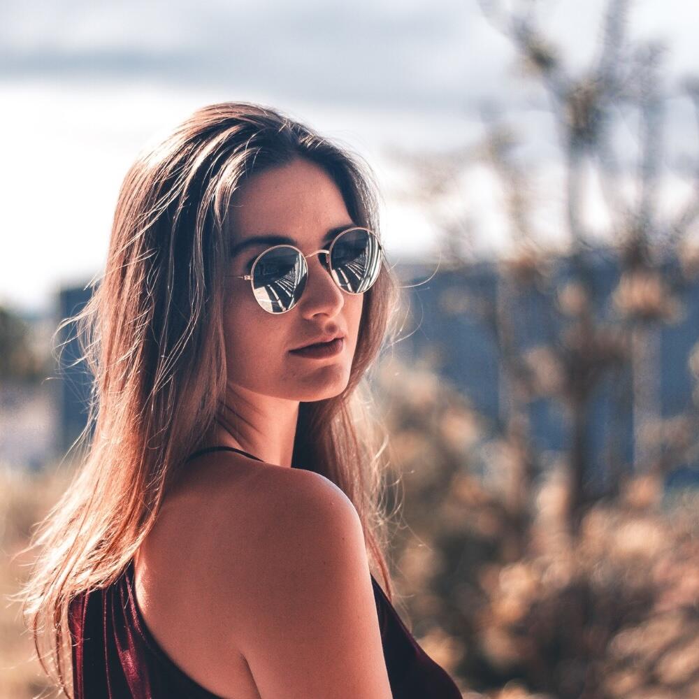 A portrait photograph of a person wearing sunglasses and looking over the shoulder